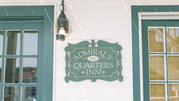 Ein Schild für das Admiral's Quarters Inn mit Vintage-Design, das über einem Fenster mit einer grünen Tür angebracht ist.
