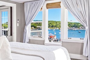 Ein Hotelzimmer mit Bett, Blick auf einen Yachthafen und einem Balkon mit Geländer.