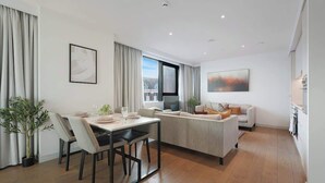 Uma sala de estar moderna com sofá, mesa de jantar com cadeiras, televisão e janela com cortinas.