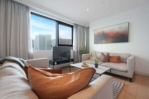 Ein modernes Wohnzimmer mit einer Couch, einem Couchtisch, einem Fernseher und einem großen Fenster.