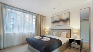 Quarto de hotel moderno com uma cama grande, mesa de cabeceira, espelho e obras de arte na parede.