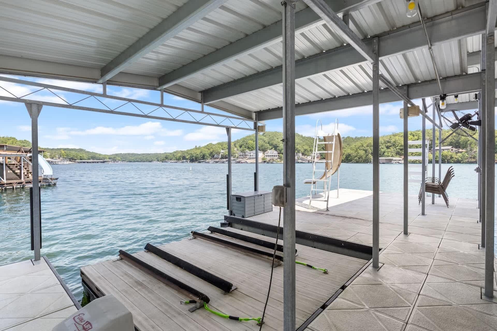 A covered dock with a view of a lake, a lifeguard stand, and a boat ramp.