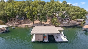 A docked houseboat with a covered deck, surrounded by trees and a small dock area. - Eagle Ridge Retreat - Dock, Hot Tub & Game Room (Gravois Mills)
