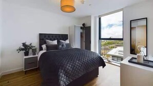 A modern bedroom with a large bed, a bedside table, a nightstand, a mirror, and a view of the outdoors. - 2 Bed Flat Near City Centre with Free Parking (Stretford)