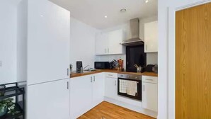 A modern kitchen with white cabinets, a black microwave, and a wooden floor. - 2 Bed Flat Near City Centre with Free Parking (Stretford)