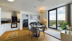 A modern interior with a dining area, kitchen, and large windows offering a city view. - 2 Bed Flat Near City Centre with Free Parking (Stretford)