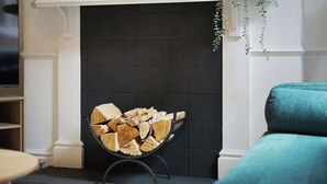 A fireplace with a log fire, a teal armchair, and a patterned rug. - Charming 4BR Retreat in Hull | Sleeps 8 | by Stay With Us (Kingston upon Hull)