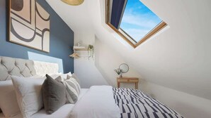 A bedroom with a bed, a headboard, a bedside table, a wall-mounted shelf, and a window. - Charming 4BR Retreat in Hull | Sleeps 8 | by Stay With Us (Kingston upon Hull)
