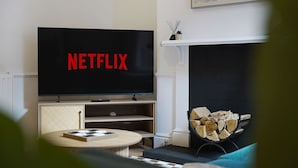 A living room with a flat-screen TV displaying 'NETFLIX,' a fireplace, and a stack of firewood. - Charming 4BR Retreat in Hull | Sleeps 8 | by Stay With Us (Kingston upon Hull)