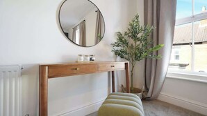 A room with a wooden console table, a round mirror, a potted plant, a window with curtains, and a radiator. - Charming 4BR Retreat in Hull | Sleeps 8 | by Stay With Us (Kingston upon Hull)