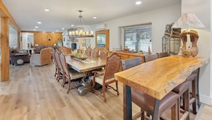 A spacious living area with a wooden dining table, comfortable seating, and a modern kitchen in the background. - Incredible retreat on the Guadalupe River (Hunt)