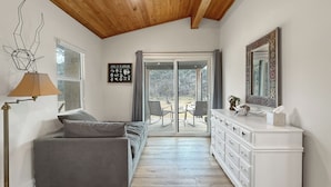 A room with a wooden ceiling, a grey sofa, a white dresser, and a large window with a view of the outdoors. - Incredible retreat on the Guadalupe River (Hunt)