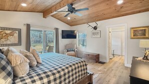 A bedroom with a checkered bedspread, a ceiling fan, a mounted TV, and a door leading to a balcony. - Incredible retreat on the Guadalupe River (Hunt)