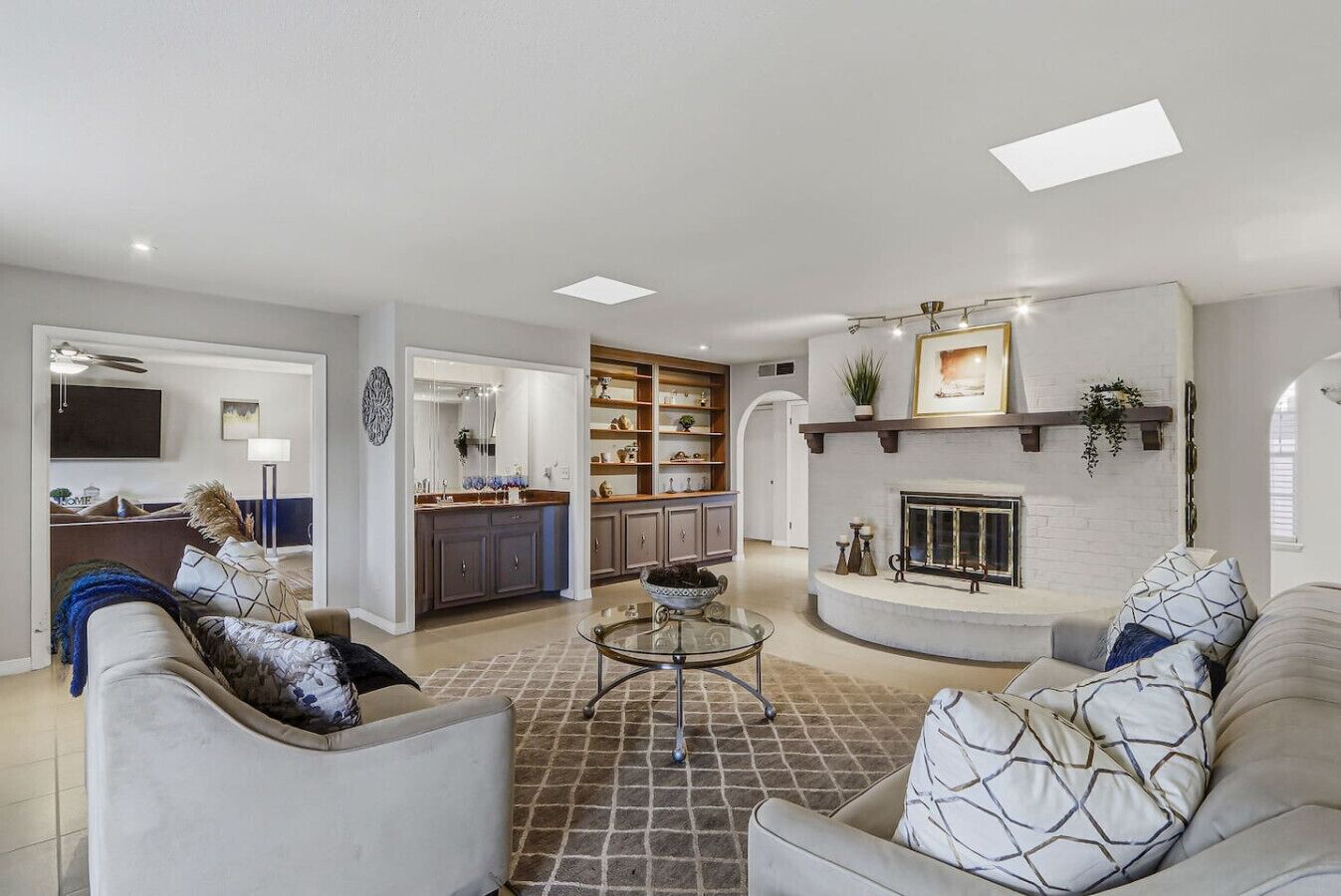 A spacious living room with a fireplace, a kitchen with open shelving, and a dining area with a glass table.