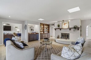 Ein geräumiges Wohnzimmer mit Kamin, eine Küche mit offenen Regalen und ein Essbereich mit Glastisch.