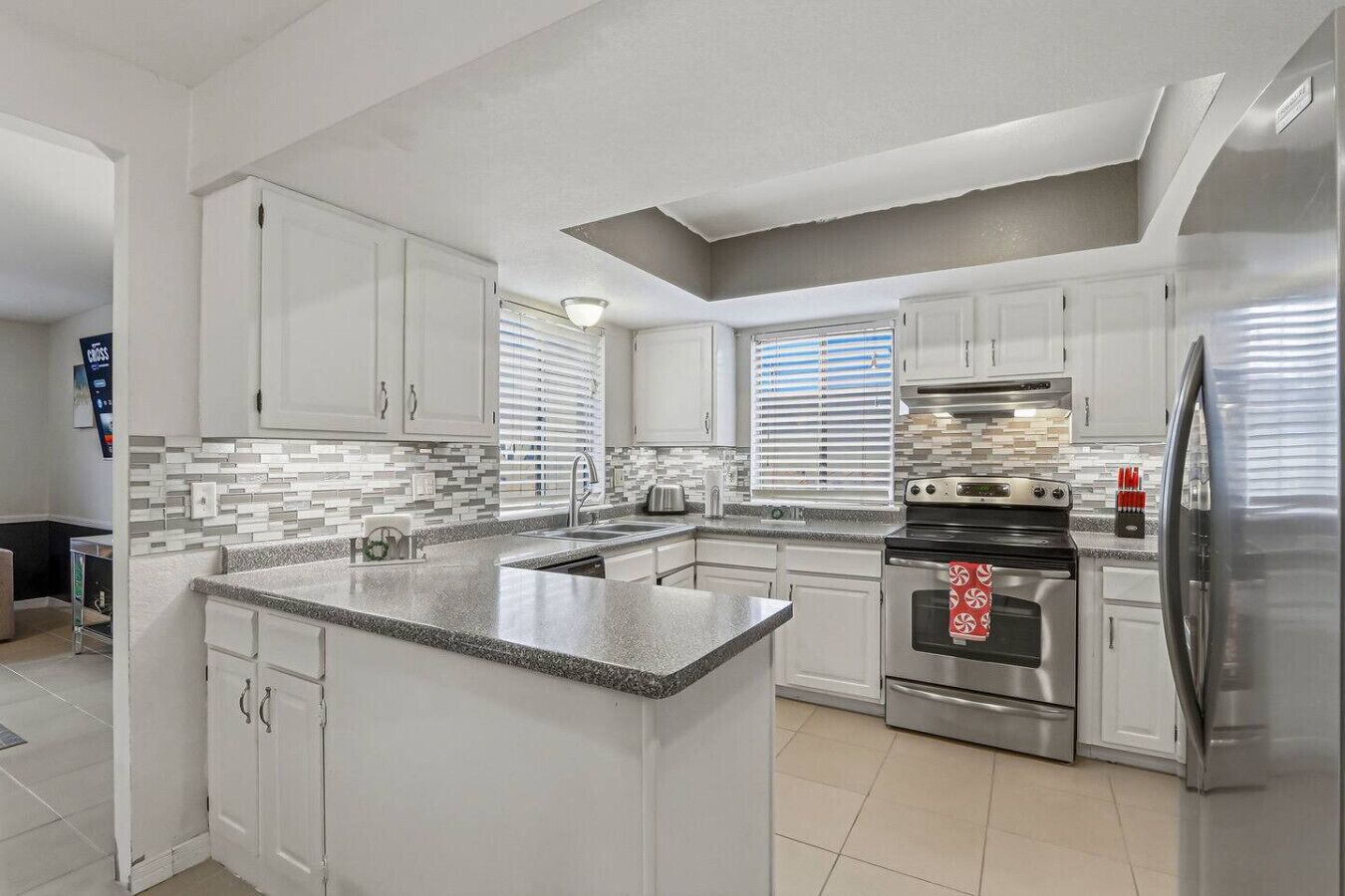 A modern kitchen with white cabinets, a granite countertop, a stainless steel oven, and a refrigerator.