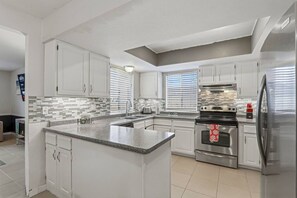 Eine moderne Küche mit weißen Schränken, einer Arbeitsplatte aus Granit, einem Edelstahlbackofen und einem Kühlschrank.