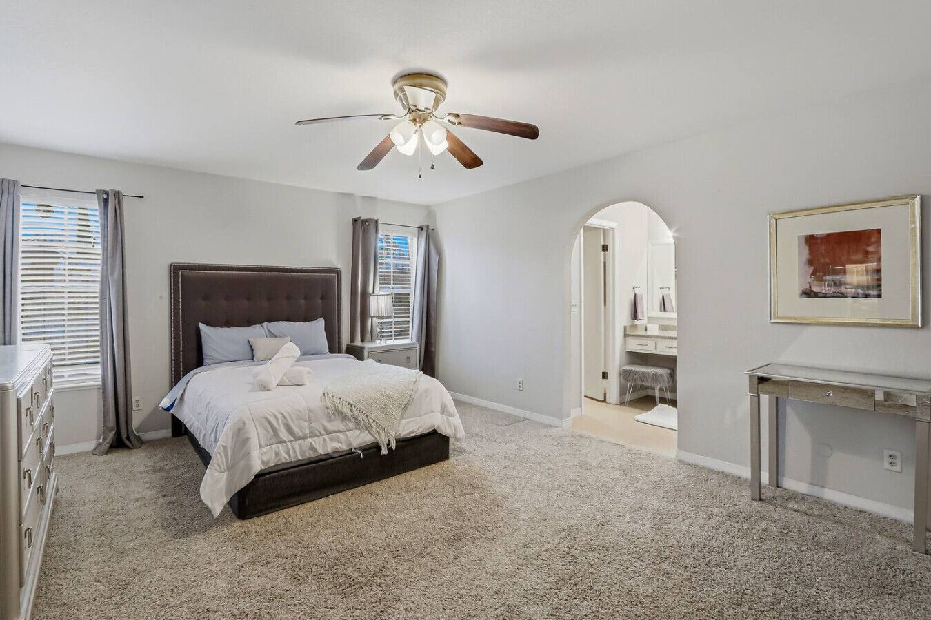 A bedroom with a bed, a ceiling fan, a dresser, and a console table.