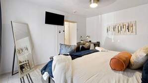 Une chambre à coucher moderne avec un lit, un bureau, une chaise, un miroir et un téléviseur.