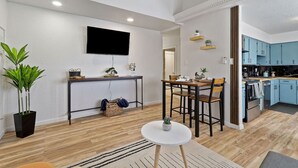 Une cuisine moderne avec des meubles bleus, un coin repas avec une table et des chaises, et un téléviseur fixé au mur.