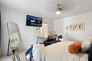 Une chambre moderne comprenant un lit, un bureau, une chaise, un grand miroir et un téléviseur fixé au mur qui affiche l’interface d’un service de diffusion en continu.