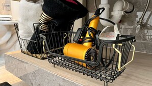 Un comptoir de cuisine sur lequel se trouve un panier en fil métallique noir contenant un appareil jaune, un chapeau noir et une serviette blanche.