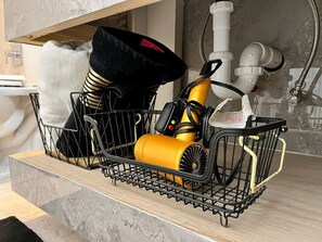A kitchen counter with a black wire basket holding a yellow appliance, a black hat, and a white towel. - Medical Stay 2BR | Central El Paso Near Hospitals (El Paso)
