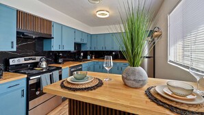 Une cuisine moderne avec des meubles bleus, un plan de travail en bois et un îlot central agrémenté d’un vase de plantes vertes.