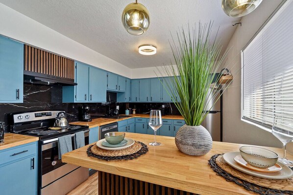 A modern kitchen with blue cabinets, a wooden countertop, and a central island with a vase of green plants. - Medical Stay 2BR | Central El Paso Near Hospitals (El Paso)