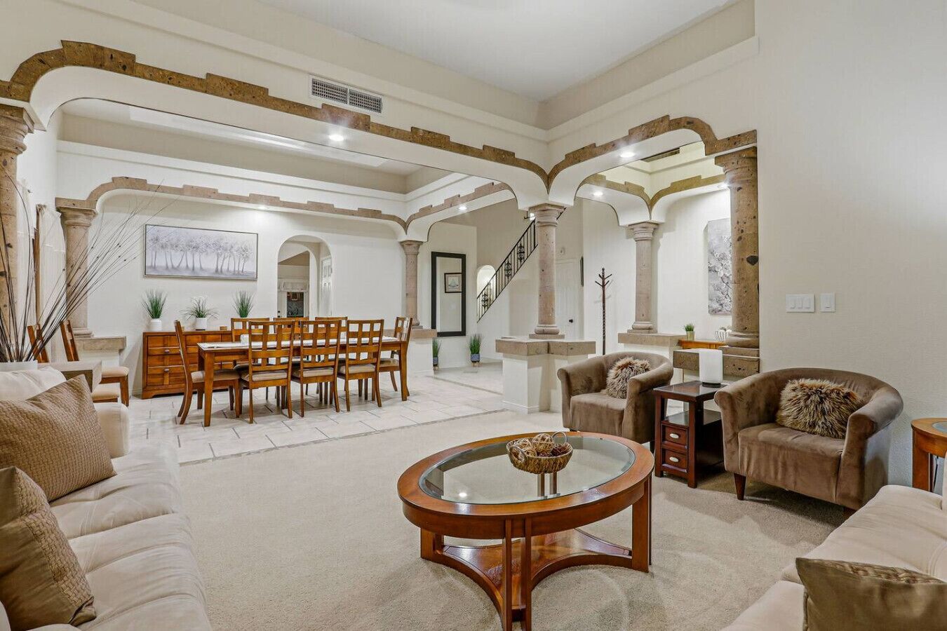 A spacious living room with a dining area, featuring a staircase, wooden furniture, and a large painting.
