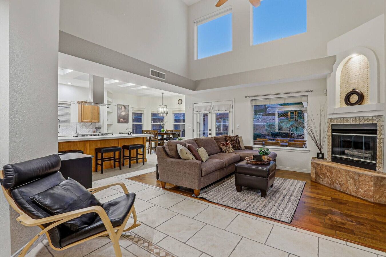 A spacious living area with a sofa, a coffee table, and a fireplace. There is a kitchen in the background with a bar and chairs.