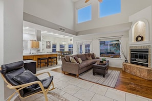 A spacious living area with a sofa, a coffee table, and a fireplace. There is a kitchen in the background with a bar and chairs. - Eagle Point Mountain View Retreat w Pool (El Paso)