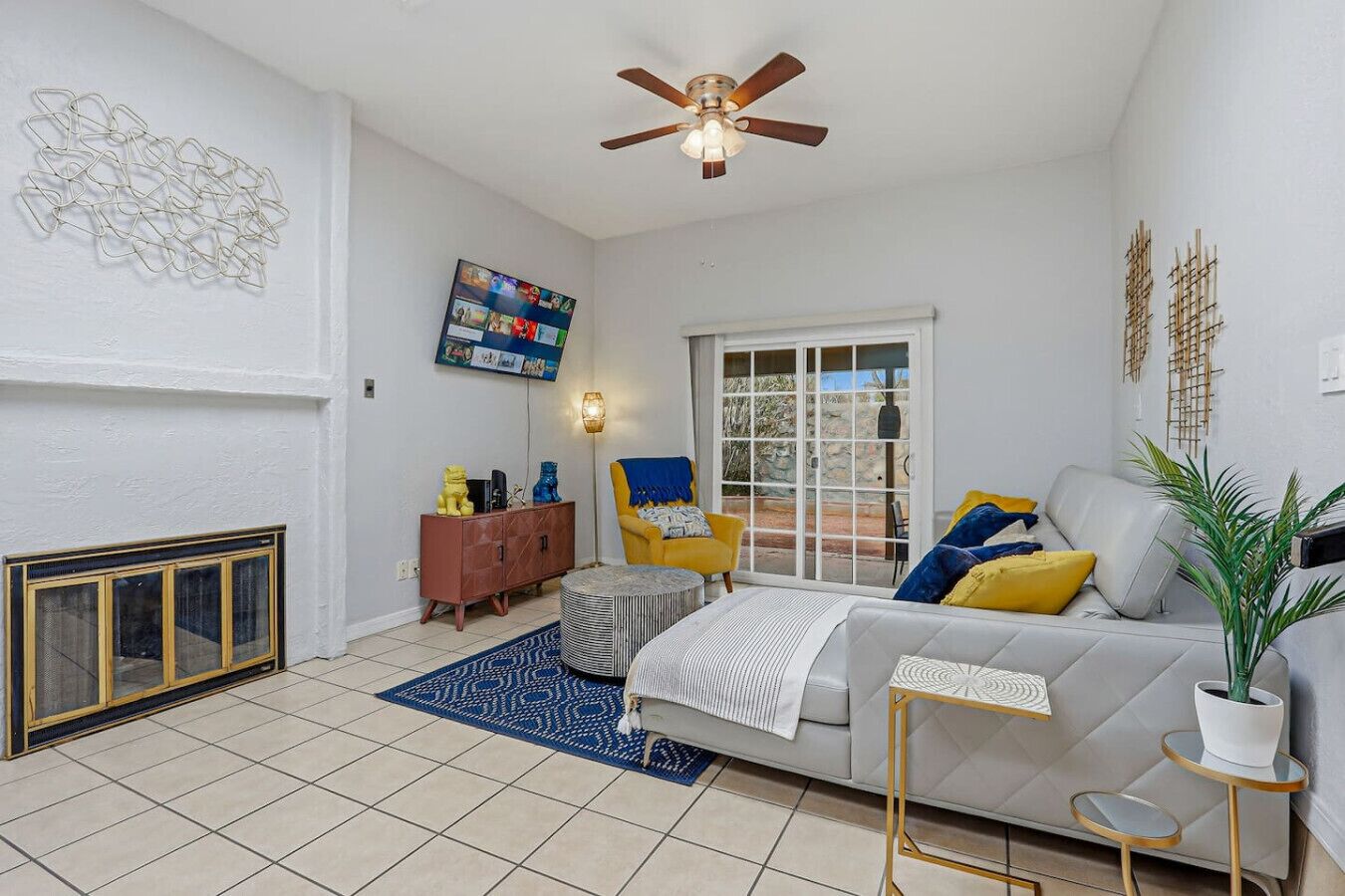 A living room with a fireplace, a ceiling fan, a television, and a large window.