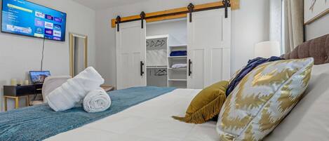 A hotel room with a bed, a TV mounted on the wall, a desk with a laptop, and a wardrobe with sliding doors.