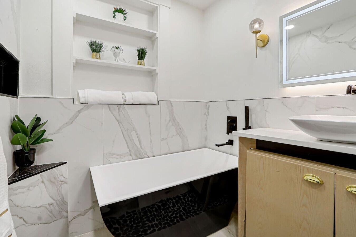 Un bagno moderno con un lavabo in marmo bianco, una vasca da bagno indipendente e uno scaffale con piante in vaso.