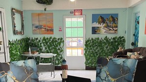 Un coin repas avec une table ronde en verre entourée de chaises bleues à revêtement, un petit phare décoratif en guise de centre de table, et une vue sur l’espace repas à travers une porte en verre.