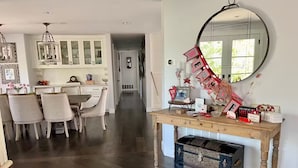 Un coin repas avec une table et des chaises en bois, une cuisine avec des meubles blancs et un miroir au mur.