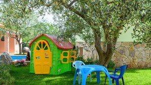 A colorful playhouse with a red roof and yellow door, surrounded by a stone wall and a large tree. - Stunning home in Peruski (Peruski)
