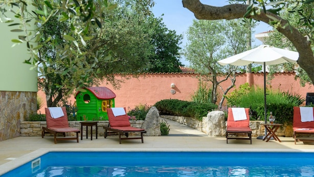 A poolside area with lounge chairs, a small playhouse, and a stone wall. - Stunning home in Peruski (Peruski)