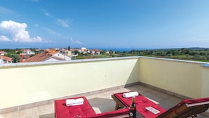 A rooftop terrace with two sunbeds, a bottle, and a book. The terrace overlooks a town with red-roofed buildings and a view of the sea. - Stunning home in Peruski (Peruski)