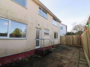 A residential building with a red and beige exterior, a wooden fence, and a paved patio area. - Piskies Magic Home (Penryn)