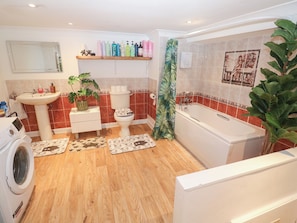 A bathroom with a sink, toilet, bathtub, and a shelf with toiletries. - Piskies Magic Home (Penryn)