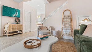 A modern living room with a curved white coffee table, a green sofa, a wicker basket, and a bookshelf. - 39 Topaz Cove•Remodeled•2 Pools•Free Beach Service•Fully-Stocked•Arcade Game (Miramar Beach)