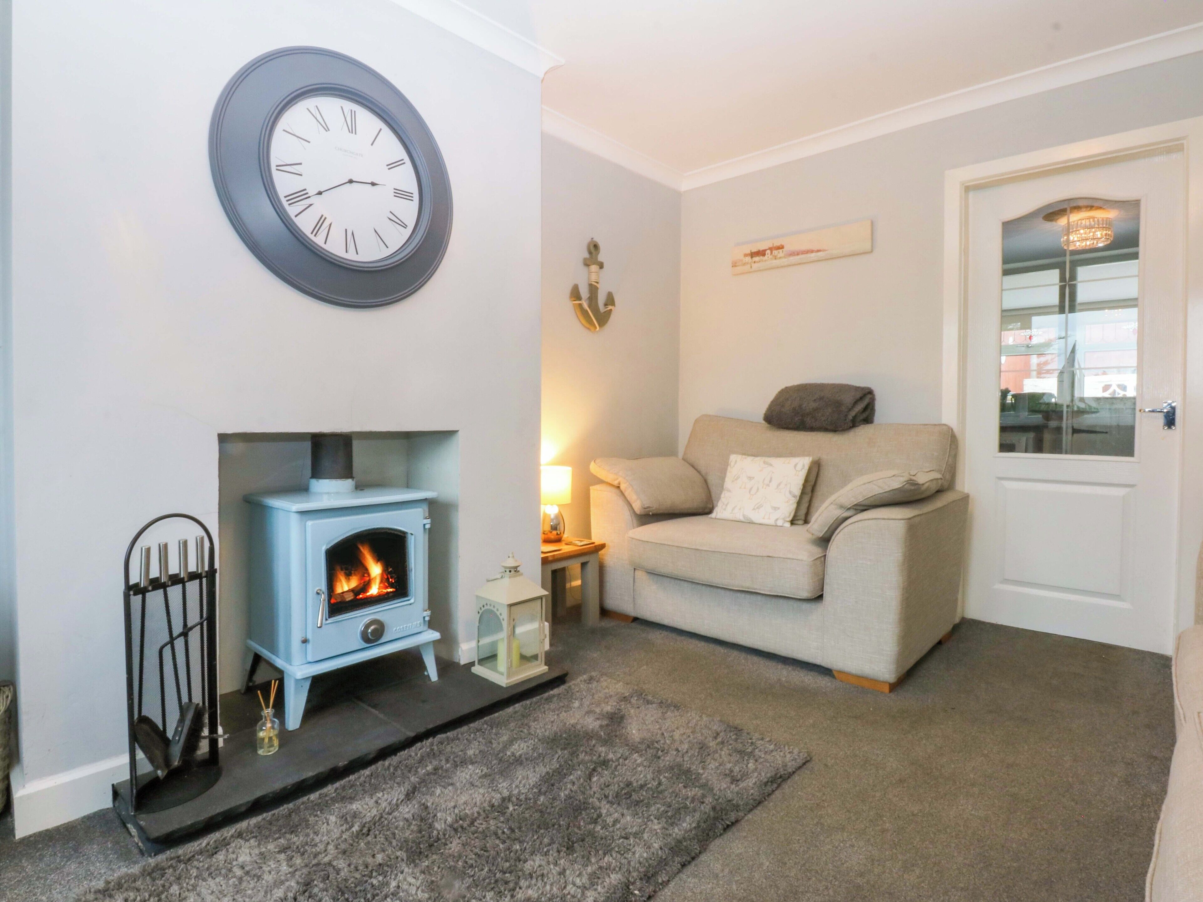 A living room with a blue wood-burning stove, a beige sofa, a clock on the wall, and a door with a window.