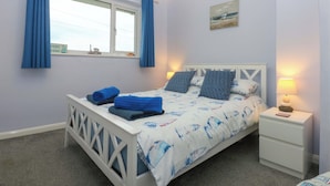 Um quarto com uma cama, uma mesa de cabeceira, uma janela com cortinas, um quadro e uma placa na janela.