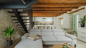 A modern living room with a sectional sofa, a staircase with black railings, and a kitchen in the background.