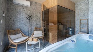 A modern bathroom with a glass-enclosed shower, two wicker chairs, a small table, a white bathtub, and a towel rack.