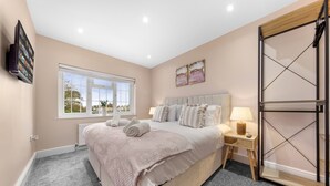 Un dormitorio con una cama grande, una mesita de noche con lámpara, un televisor montado en la pared y una ventana con vistas al exterior.