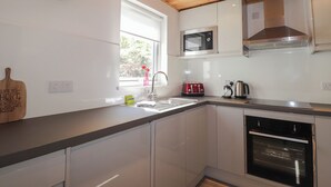A modern kitchen with white cabinets, a wooden ceiling, a microwave, a toaster, and a sink. - Tigh a Phailean (Kyle)