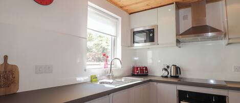 A modern kitchen with white cabinets, a wooden ceiling, a microwave, a toaster, and a sink.